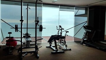 Un gimnasio con diverso equipo de ejercicio, amplias ventanas con vista al mar y una cinta de correr.