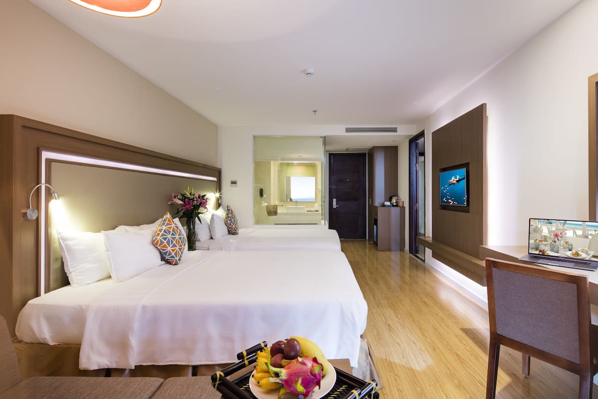 A hotel room with two beds, a desk with a laptop, a TV, and a fruit basket on the bed.