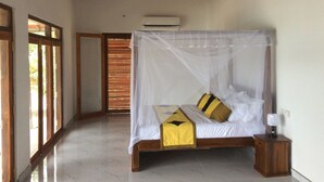 A bedroom with a bed under a mosquito net, a bedside table with a lamp, and a view through a door to a room with a wooden ceiling. - Beach Villa Lanka (Tangalle)