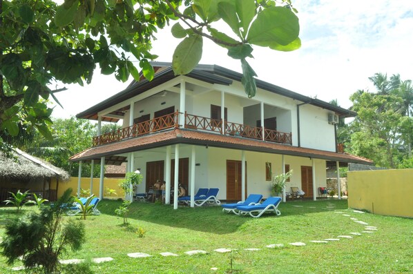 A two-story building with a balcony, a thatched-roof structure, and a well-maintained lawn with lounge chairs. - Beach Villa Lanka (Tangalle)