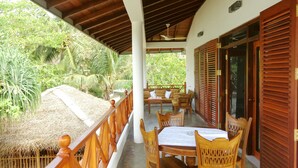 A covered outdoor area with a wooden table and chairs, a thatched roof, and a view of lush greenery. - Beach Villa Lanka (Tangalle)