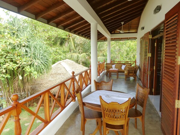 A covered outdoor seating area with wooden furniture and a view of lush greenery.
