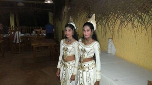 Two individuals in traditional attire standing in a room with wooden furniture and a thatched wall. - Beach Villa Lanka (Tangalle)