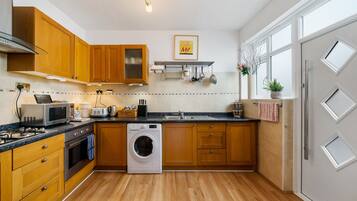 A modern kitchen with wooden cabinets, a built-in oven, a microwave, a washing machine, and a large window providing natural light.