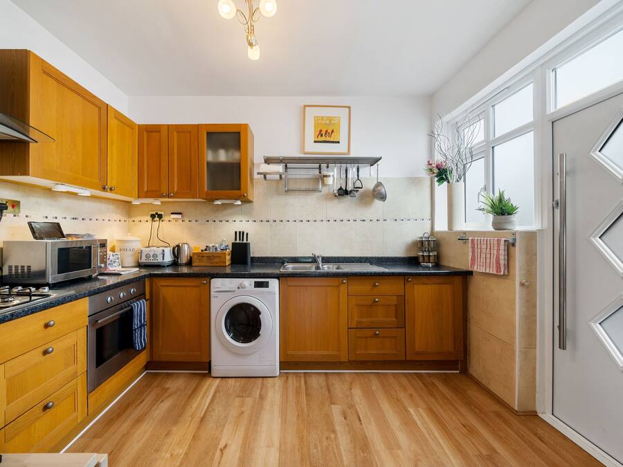 A modern kitchen with wooden cabinets, a built-in oven, a microwave, a washing machine, and a large window providing natural light.