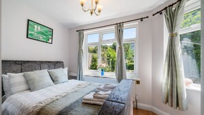Une chambre à coucher avec un grand lit, une tête de lit, une fenêtre avec des rideaux et une affiche de Wimbledon accrochée au mur.