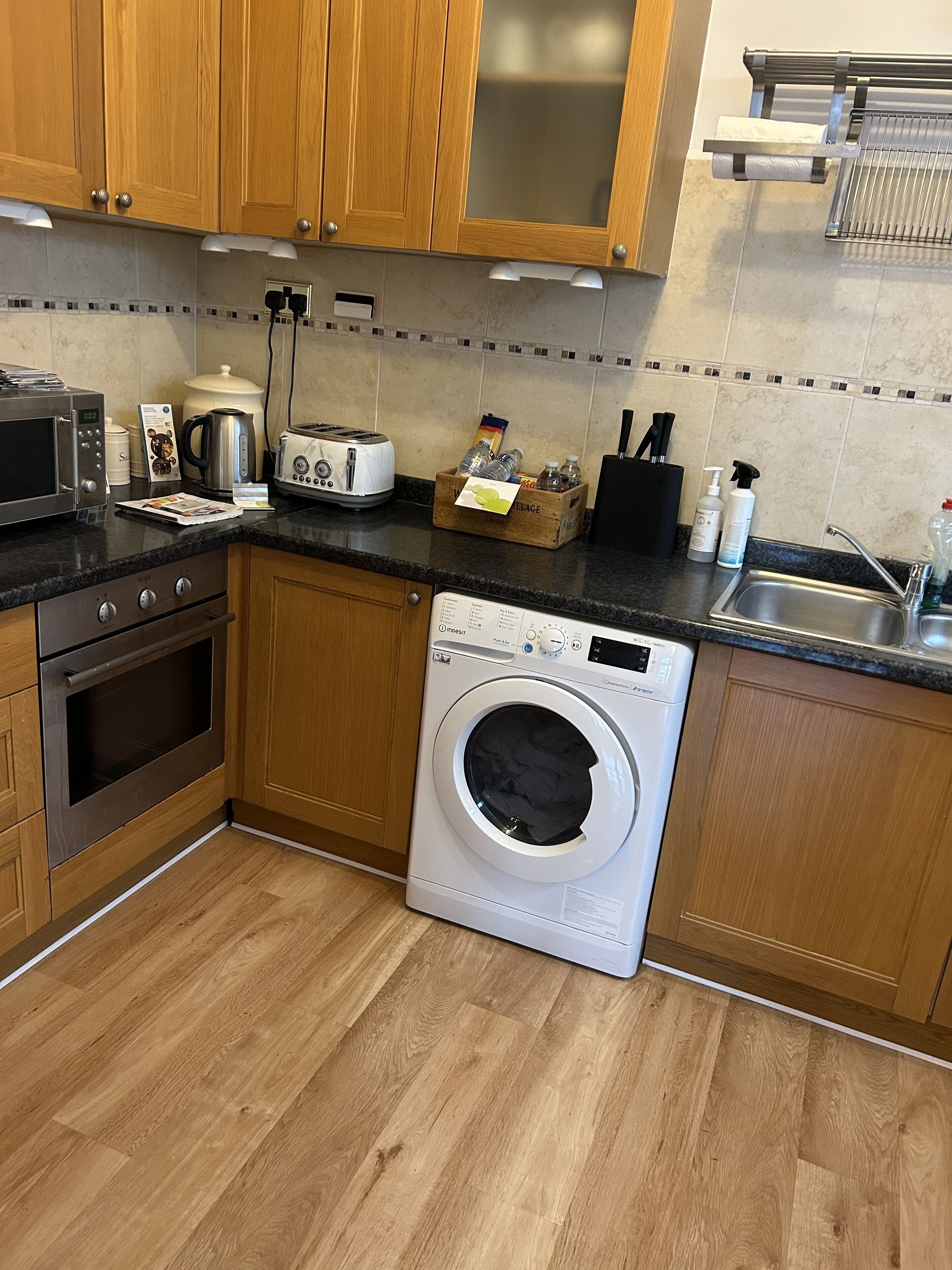 Eine Küche mit Holzschränken, einer Mikrowelle, einem Toaster, einem Wasserkocher, einer Waschmaschine und einem Spülbecken.