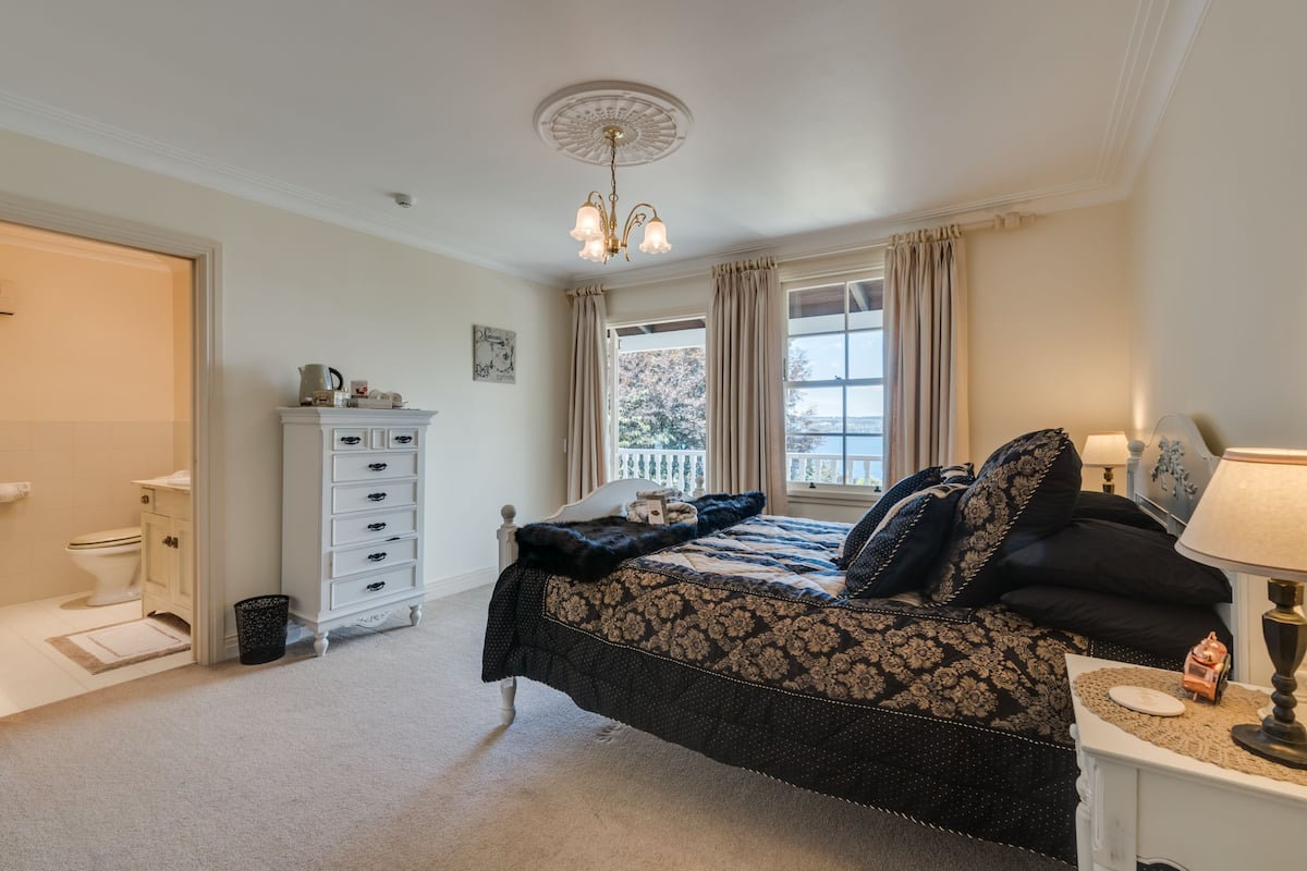 A bedroom with a bed, a nightstand, a dresser, a window with curtains, and a chandelier.