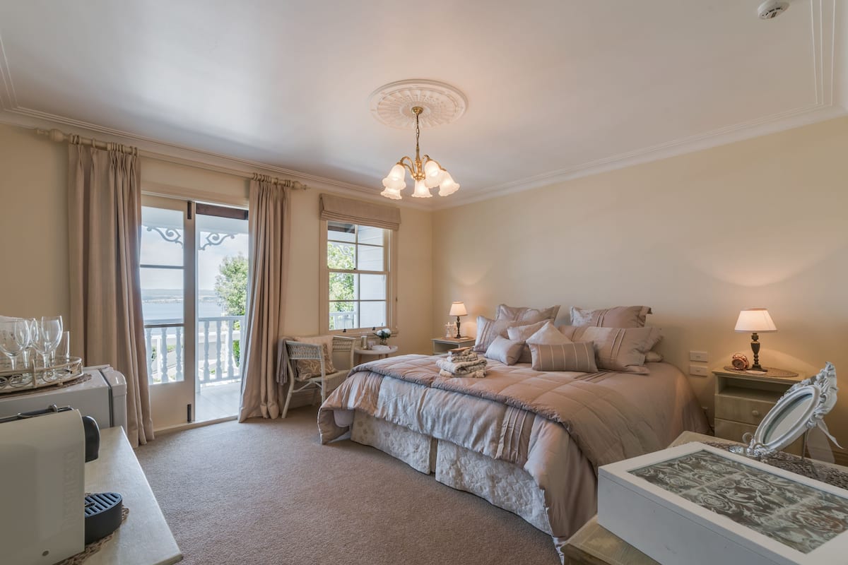 A bedroom with a large bed, two bedside tables with lamps, a dresser, a chair, and a view of the outdoors through a sliding door.