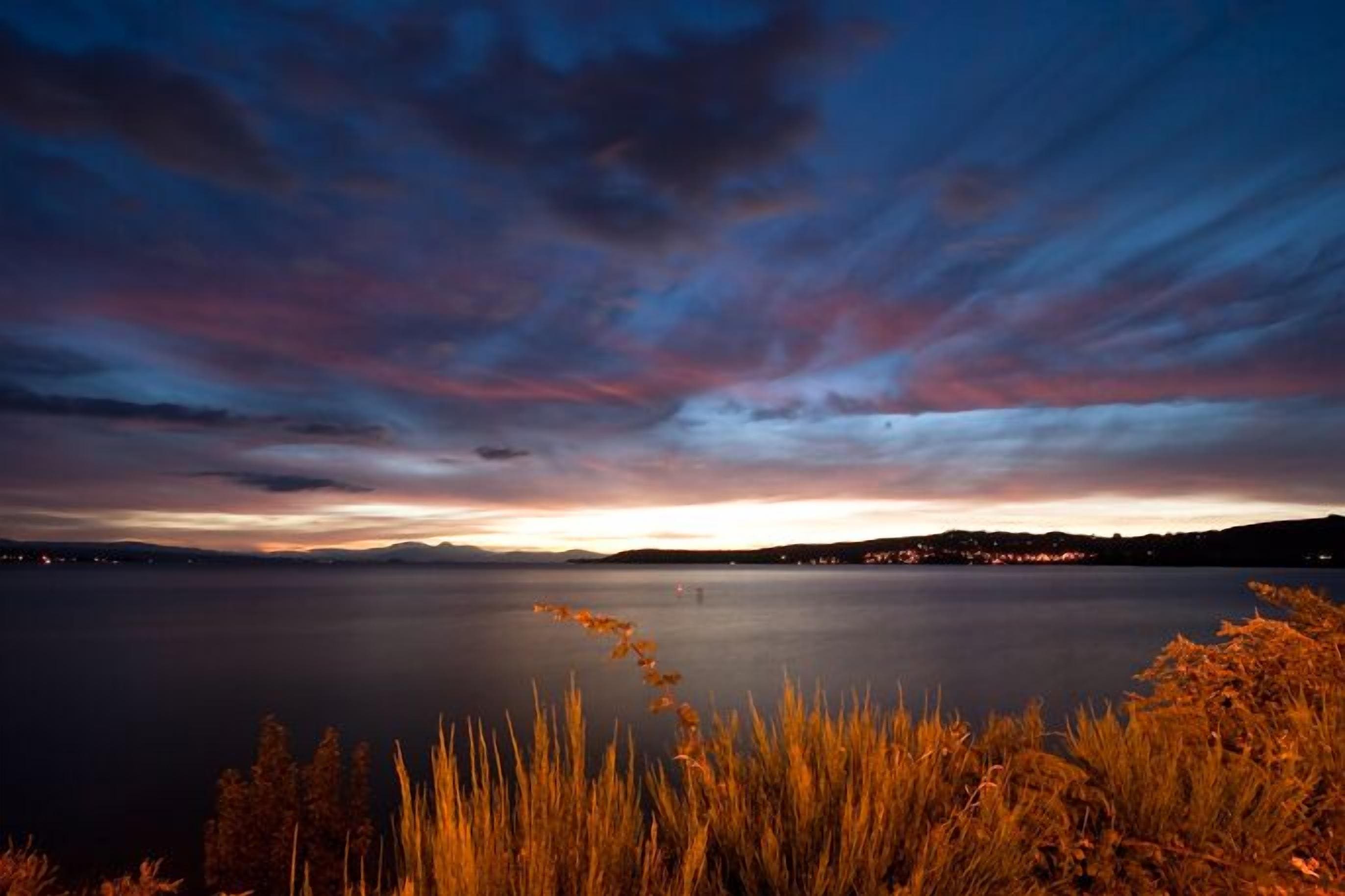 Un lac paisible au crépuscule, avec un horizon dégagé et des lumières lointaines.