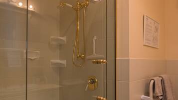 Een douche met glazen wand, een gouden douchekop en een handdoekrek met een handdoek.