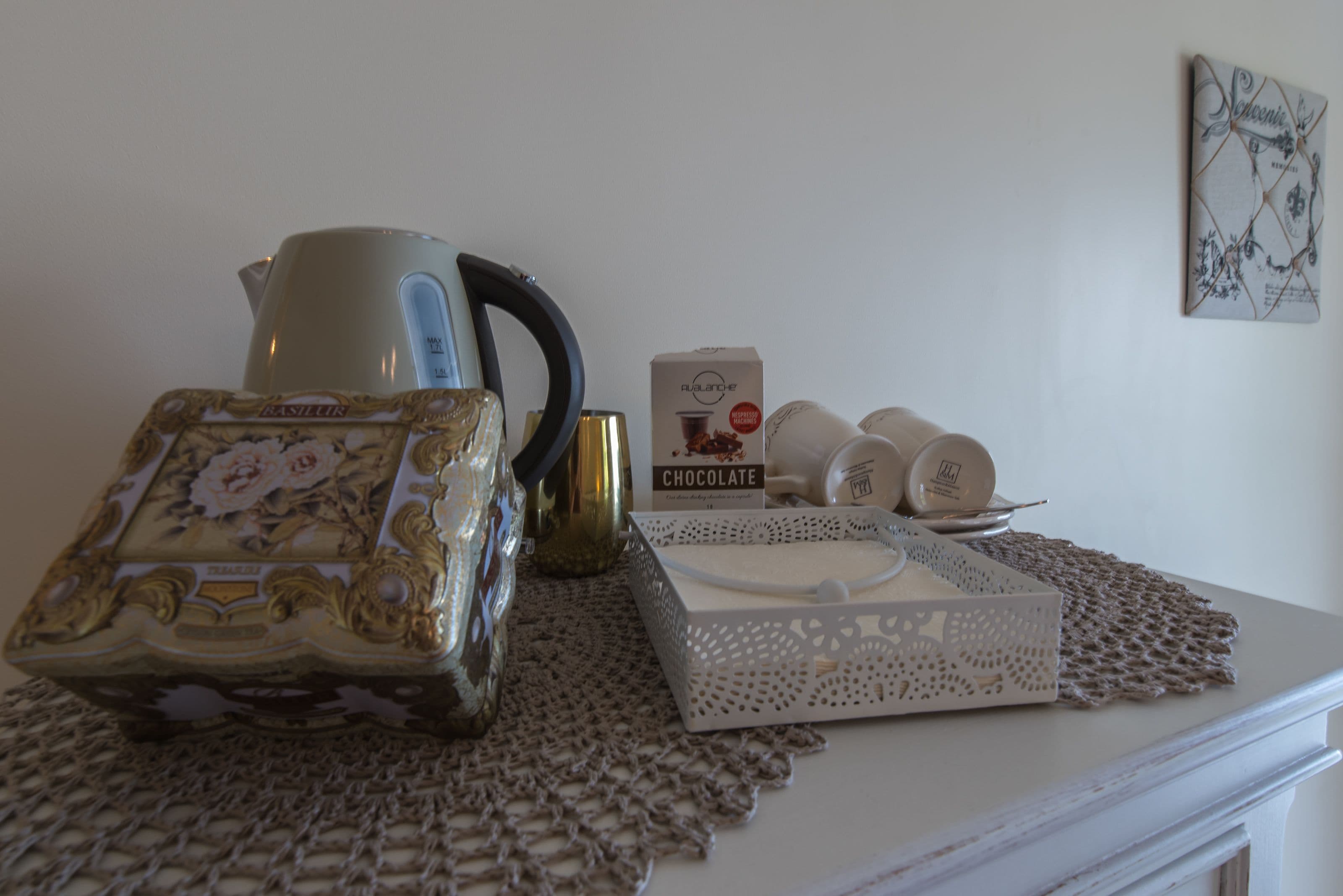 A table with a decorative box, a coffee maker, a chocolate box, and a plate with cups.