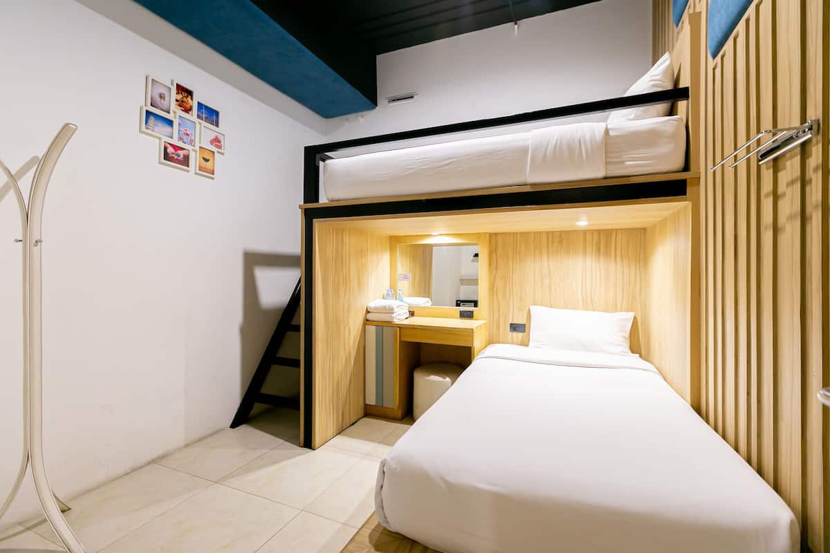 Een compacte hotelkamer met een stapelbed, een klein bureau met spiegel en een douche.
