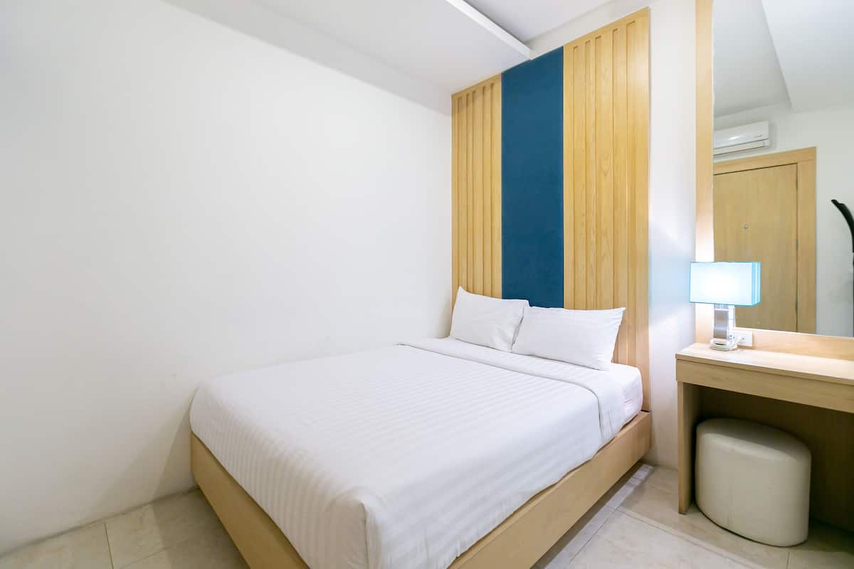 Een netjes opgemaakt bed in een kamer met een houten hoofdeinde, een klein nachtkastje met een lamp en een prullenbak.