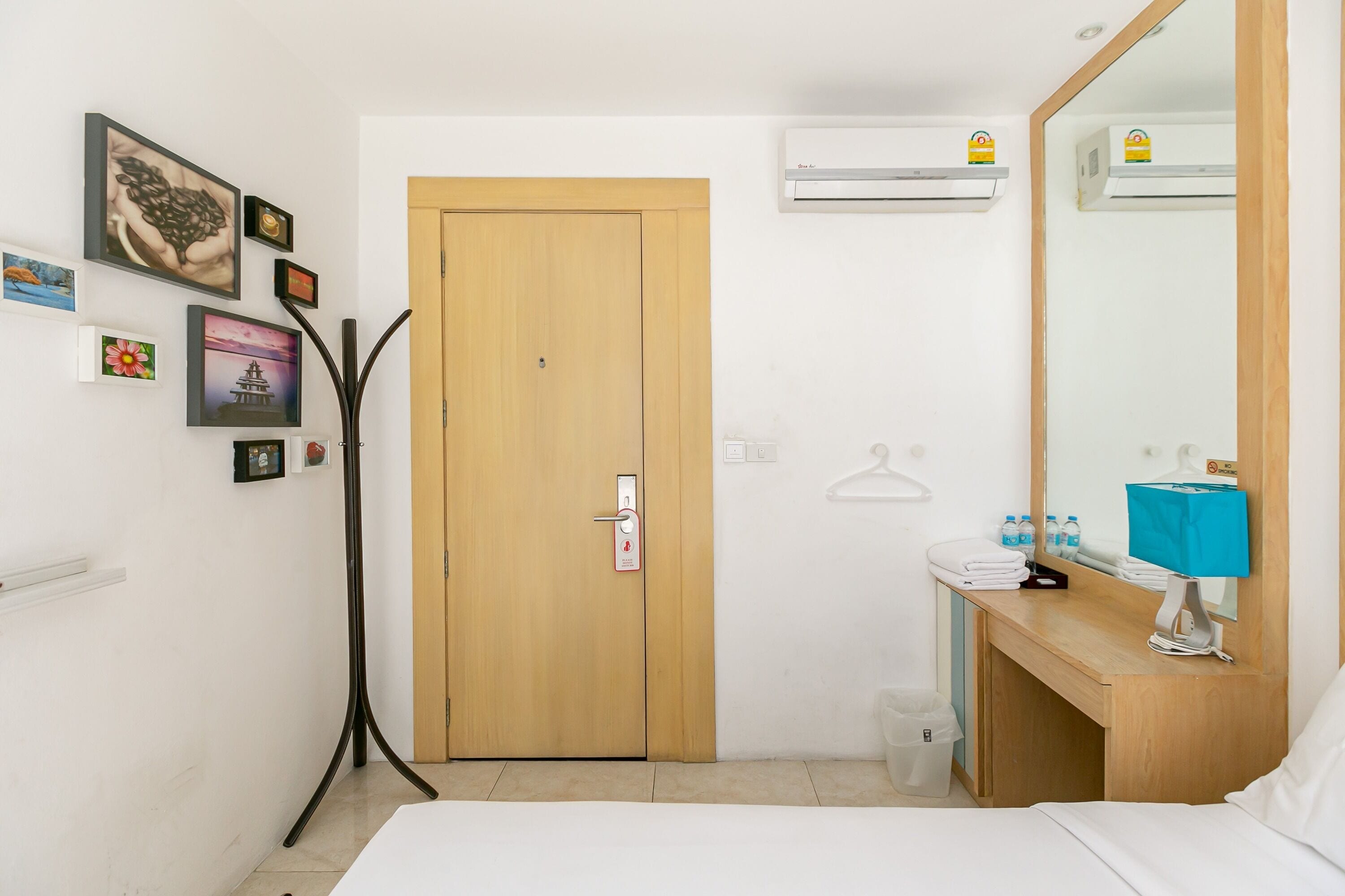 Habitación de hotel con puerta de madera, cama, mesita de noche con lámpara, espejo y aire acondicionado instalado en la pared.