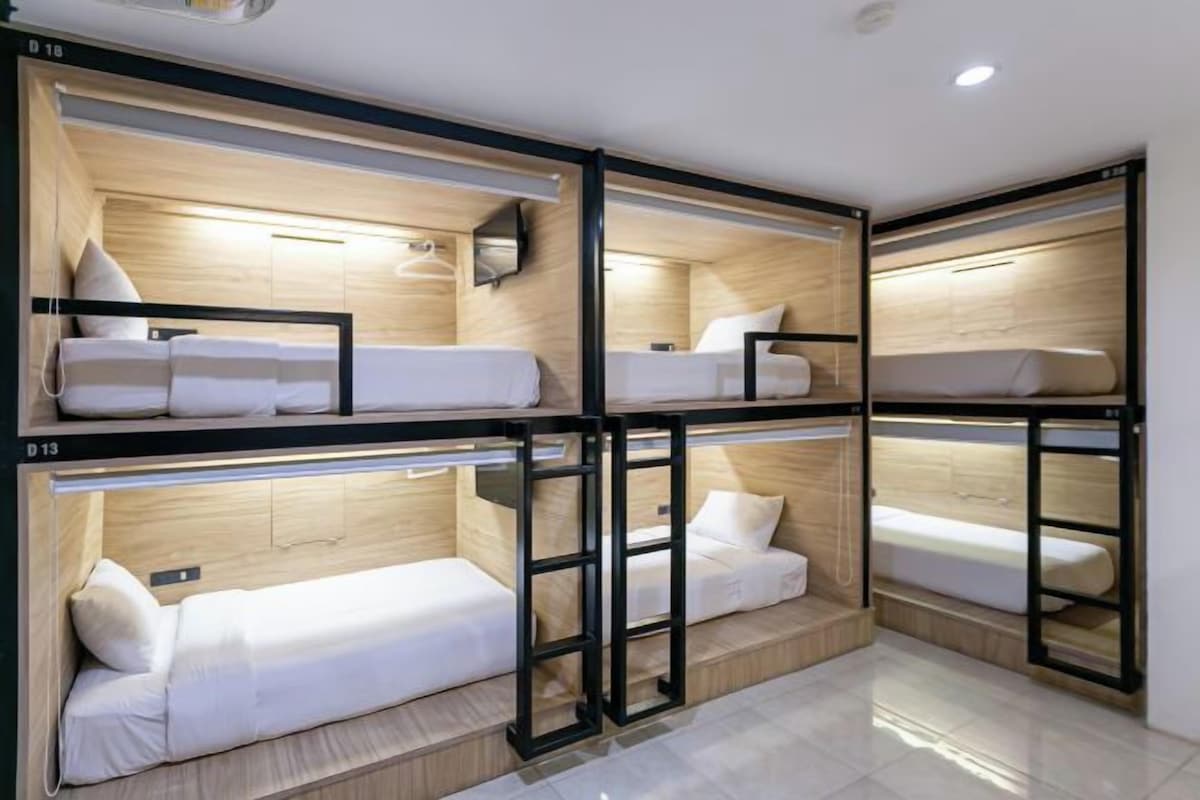 Une chambre d’hôtel avec des lits superposés, des têtes de lit en bois et une petite table de chevet avec une lampe.