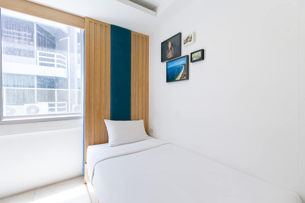 Een hotelkamer met een bed, een raam met uitzicht op een gebouw en drie ingekaderde foto's aan de muur.