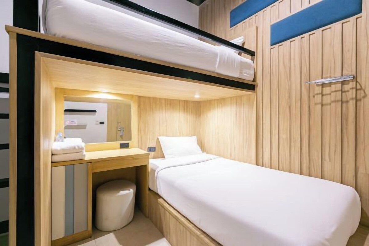Une chambre d’hôtel compacte avec un lit superposé, une petite salle de bain et un décor mural en bois.
