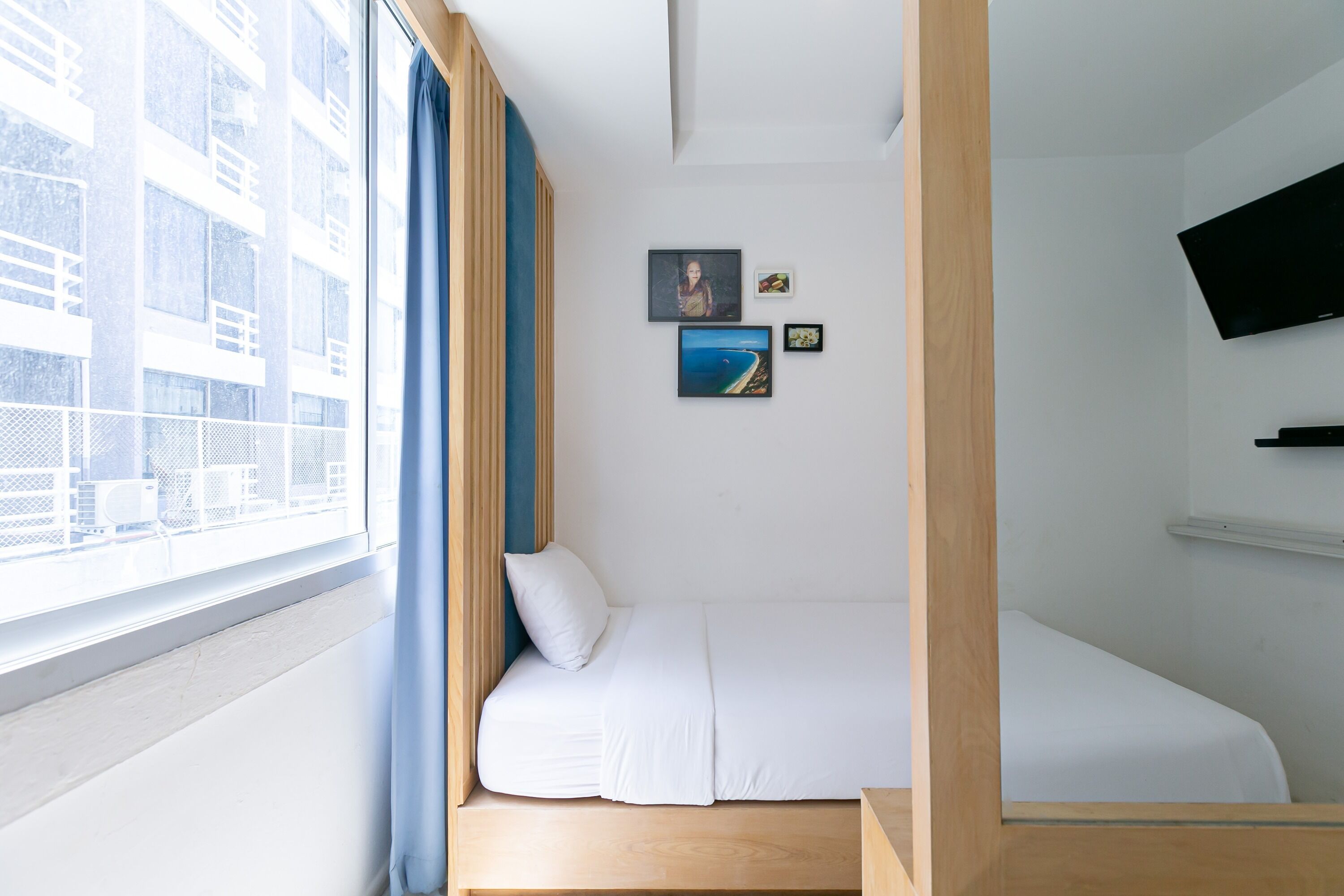 Un dormitorio pequeño con una cama, una ventana con cortinas y un televisor montado en la pared.
