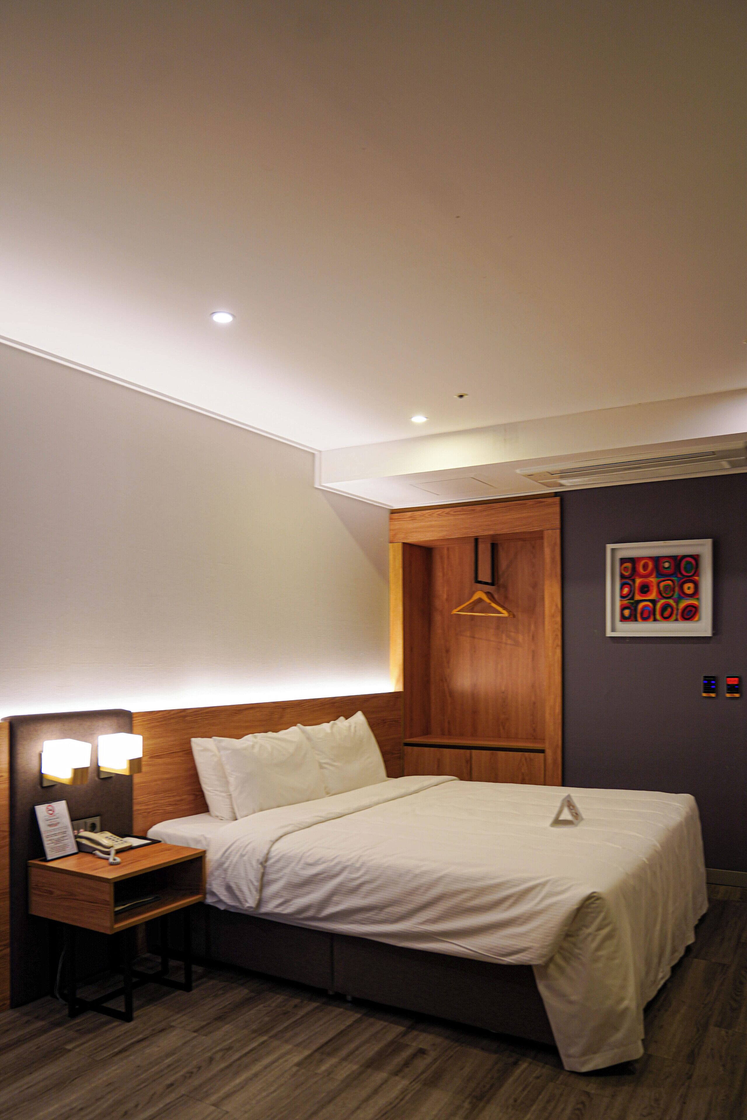 A hotel room with a bed, bedside table, lamp, and a wooden wardrobe.