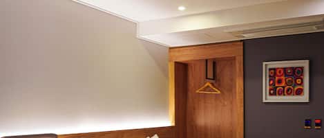 A hotel room with a bed, bedside table, lamp, and a wooden wardrobe.