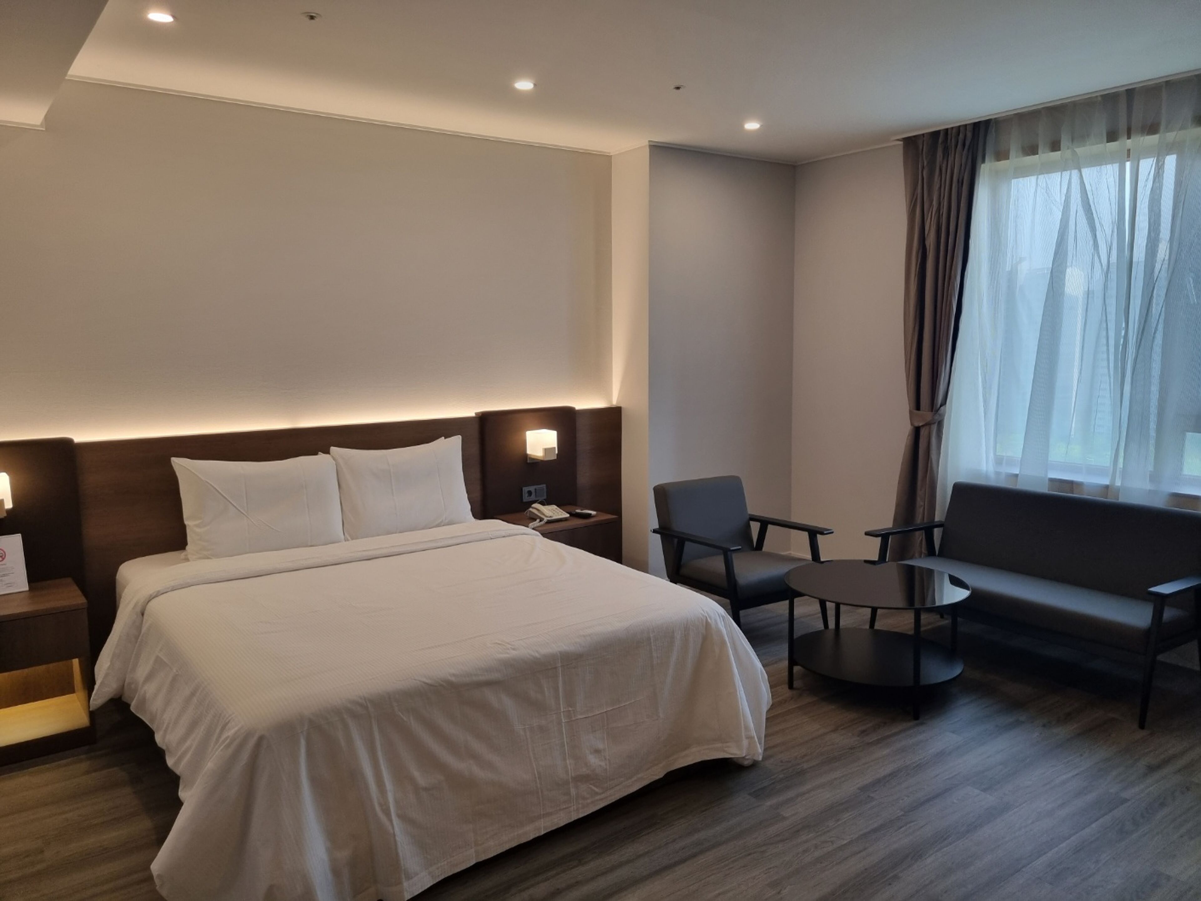 A hotel room with a bed, two chairs, a small table, a sofa, and a window with curtains.