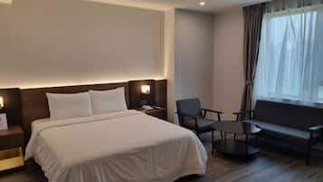 A hotel room with a bed, two chairs, a small table, a sofa, and a window with curtains.