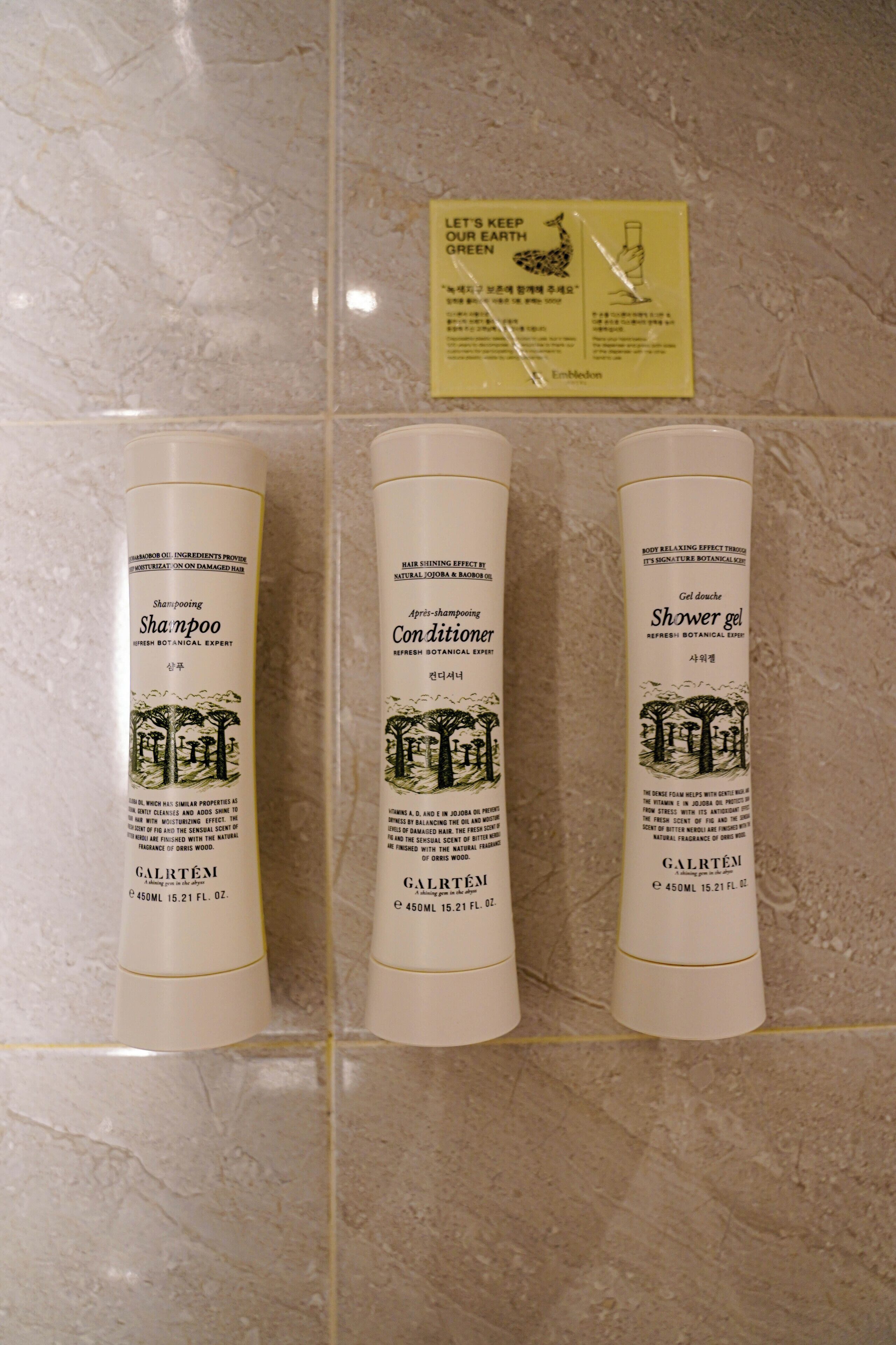 Trois bouteilles de shampoing, d’après-shampoing et de gel douche de la marque Galrtem, posées sur un sol carrelé.