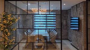 A modern dining area with a glass partition, a dining table with chairs, a vase with yellow flowers, and a mounted television on the wall. - Embledon Hotel (Ansan)
