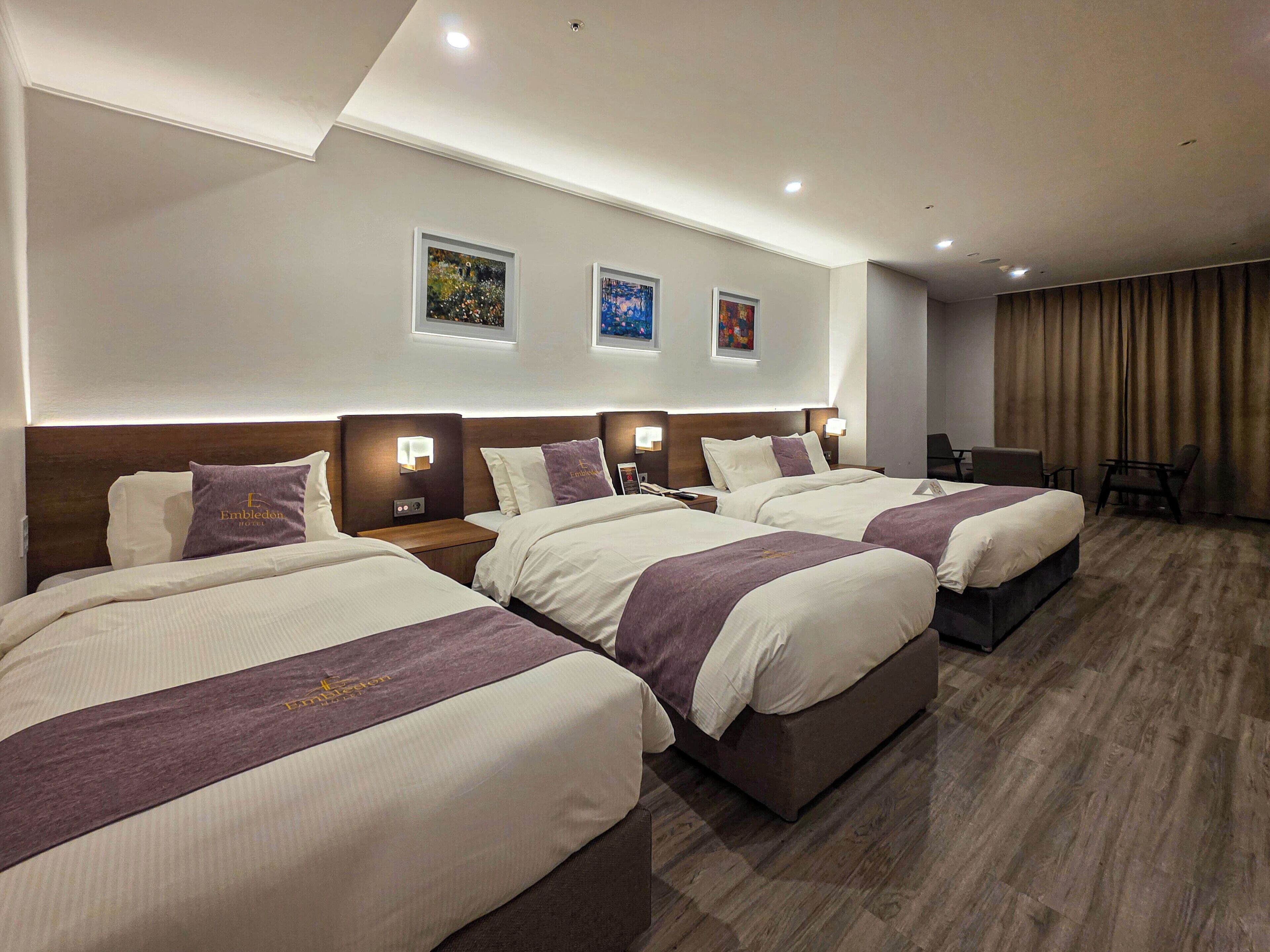 A hotel room with three beds, a desk, and a chair.