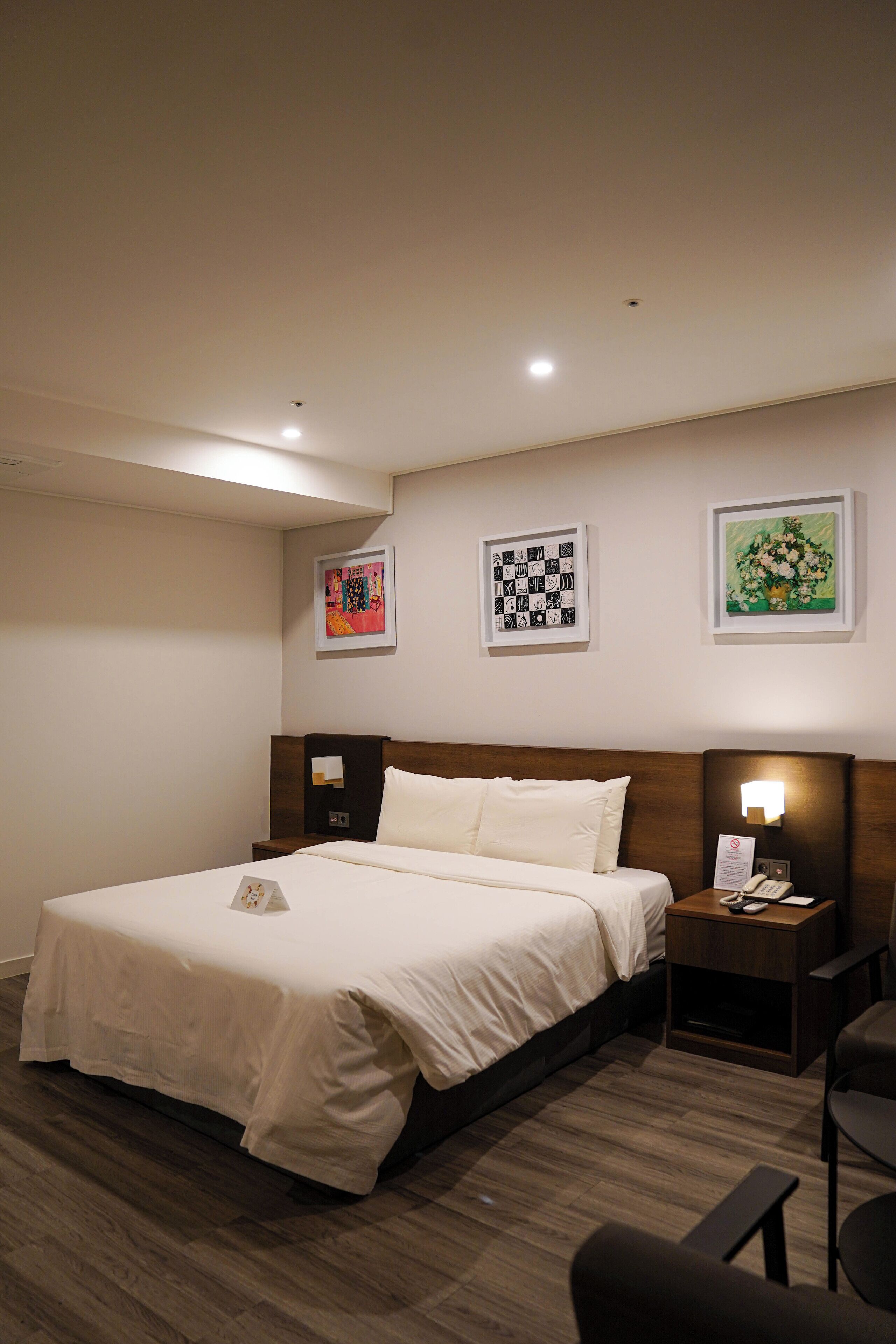Una habitació d'hotel amb un llit, taules de nit, escriptori i obra d'art a les parets.