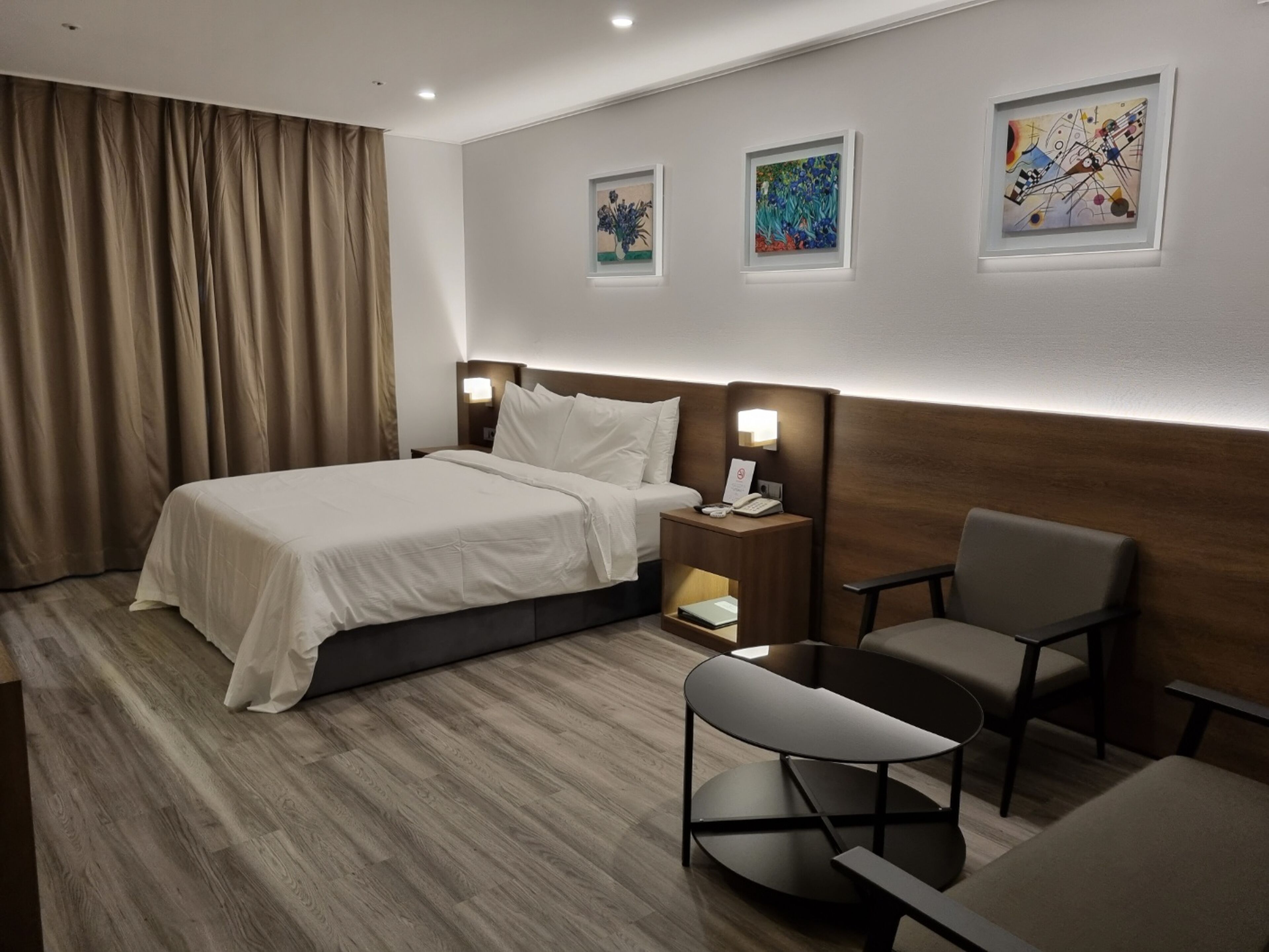 A hotel room with a bed, bedside table with a phone, a chair, and artwork on the wall.