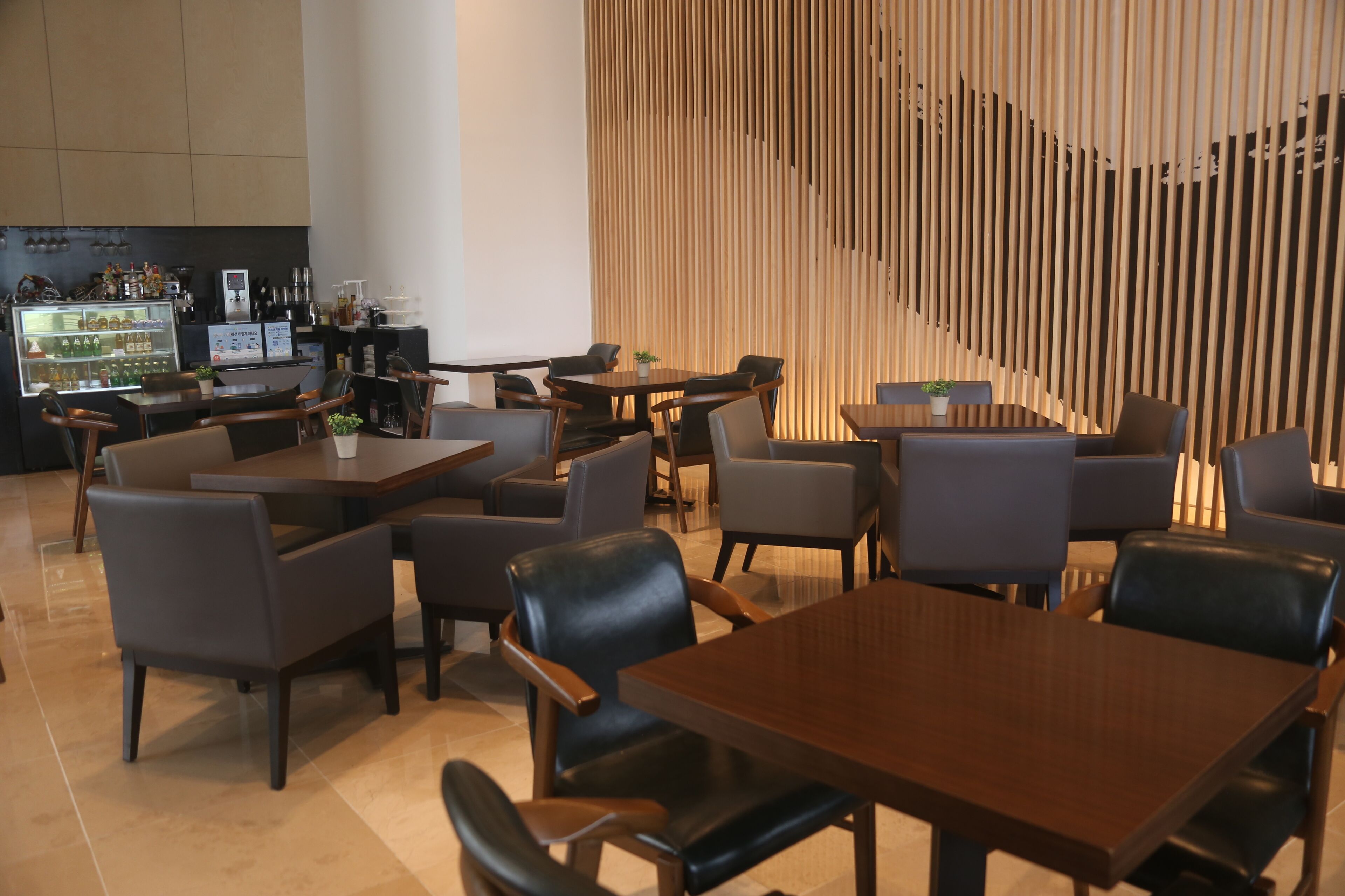 Un restaurante moderno con varias mesas y sillas, una zona de bar con un mostrador y una pared de listones de madera.