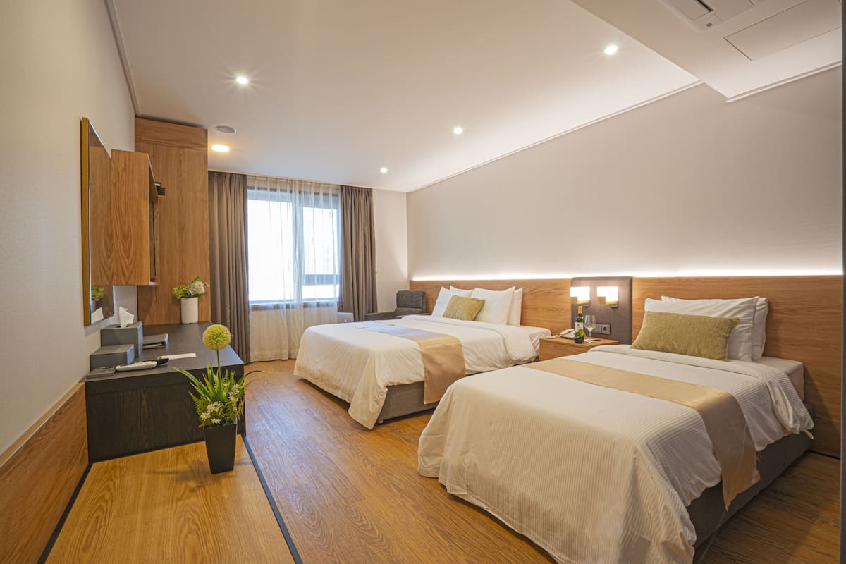 A modern hotel room with two beds, a desk, a mirror, and a potted plant.