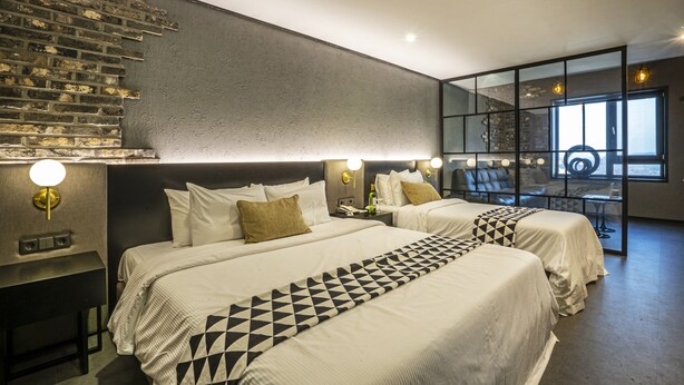 A modern hotel room with two beds, a brick wall, and a large window. - Embledon Hotel (Ansan)