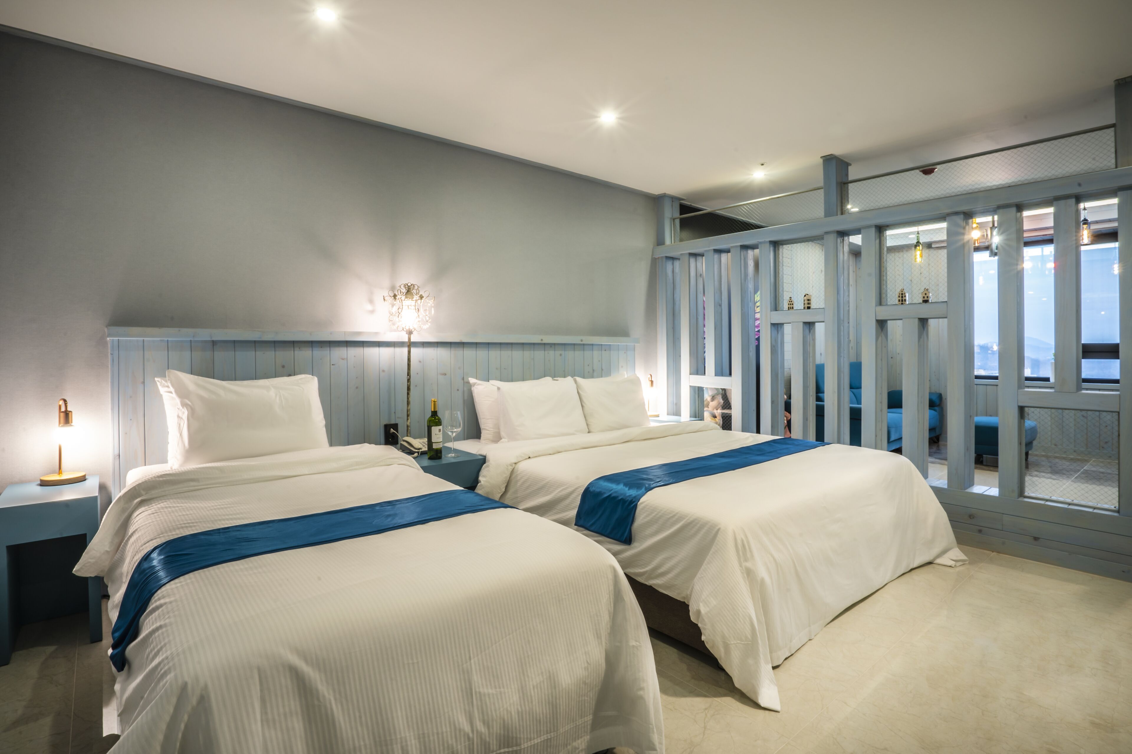 Een hotelkamer met twee bedden, een nachtkastje, een lamp en uitzicht op zee door grote ramen.