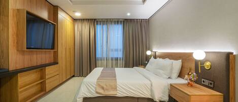 A hotel room with a bed, bedside table, lamp, and a TV mounted on the wall.