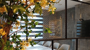 A modern interior with a dining area, a plant with yellow flowers, and a view through a glass partition. - Embledon Hotel (Ansan)