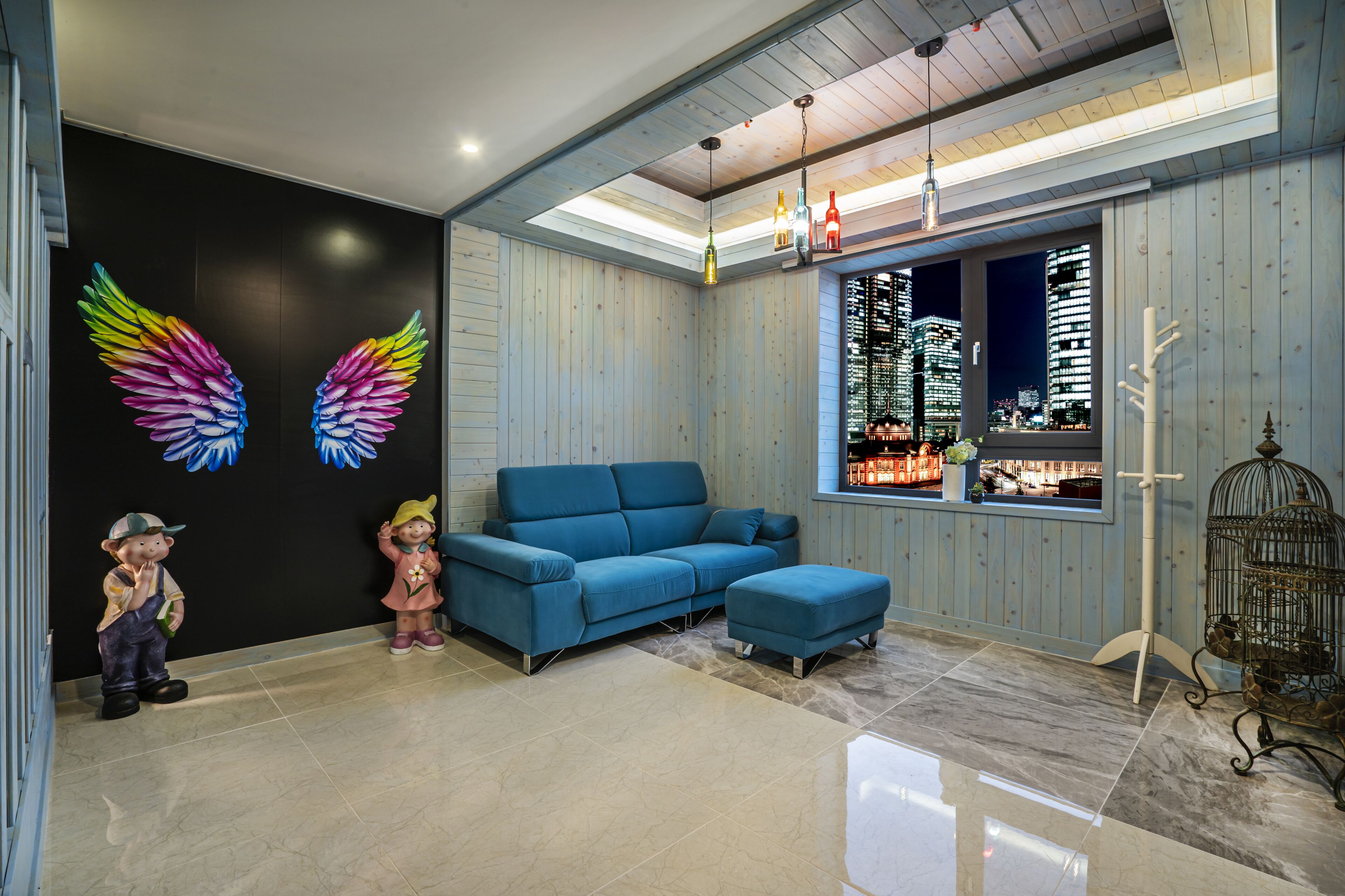 A modern living room with a blue sofa, a large window with a city view, and decorative wall art including colorful wings and figurines.