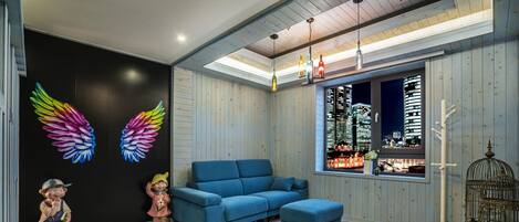 A modern living room with a blue sofa, a large window with a city view, and decorative wall art including colorful wings and figurines.