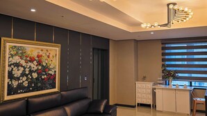 A modern living room with a black leather sofa, a marble coffee table, a large floral painting, and a unique ceiling light fixture. - Embledon Hotel (Ansan)