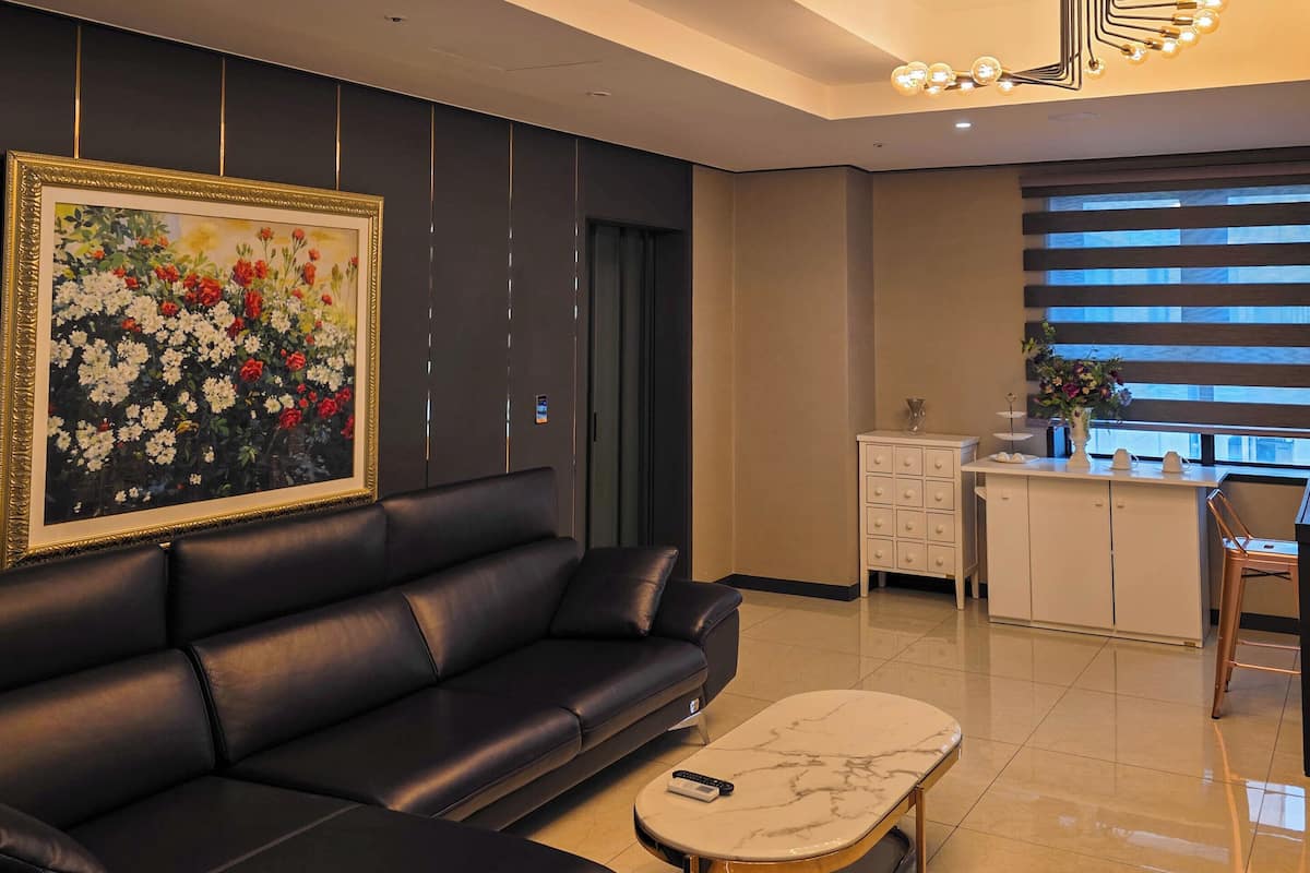 A modern living room with a black leather sofa, a marble coffee table, a large floral painting, and a unique ceiling light fixture.