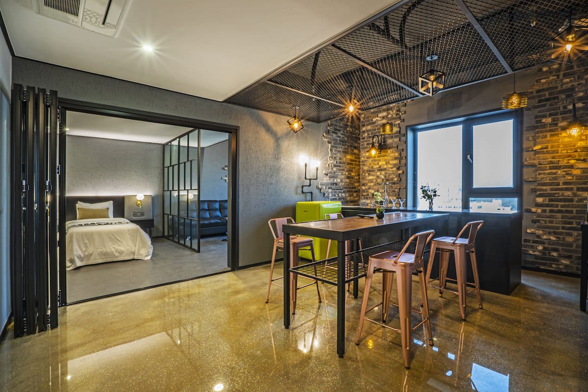 A modern interior with a polished floor, a bar area with stools, a bed, and a view through a glass door.