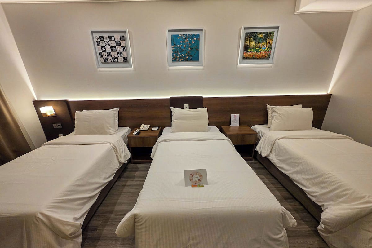 A hotel room with three single beds, a wooden headboard, a nightstand with a phone, and framed artwork on the wall.