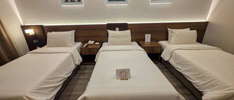 Habitación de hotel con tres camas individuales, cabecera de madera, mesita de noche con teléfono y cuadros en la pared.