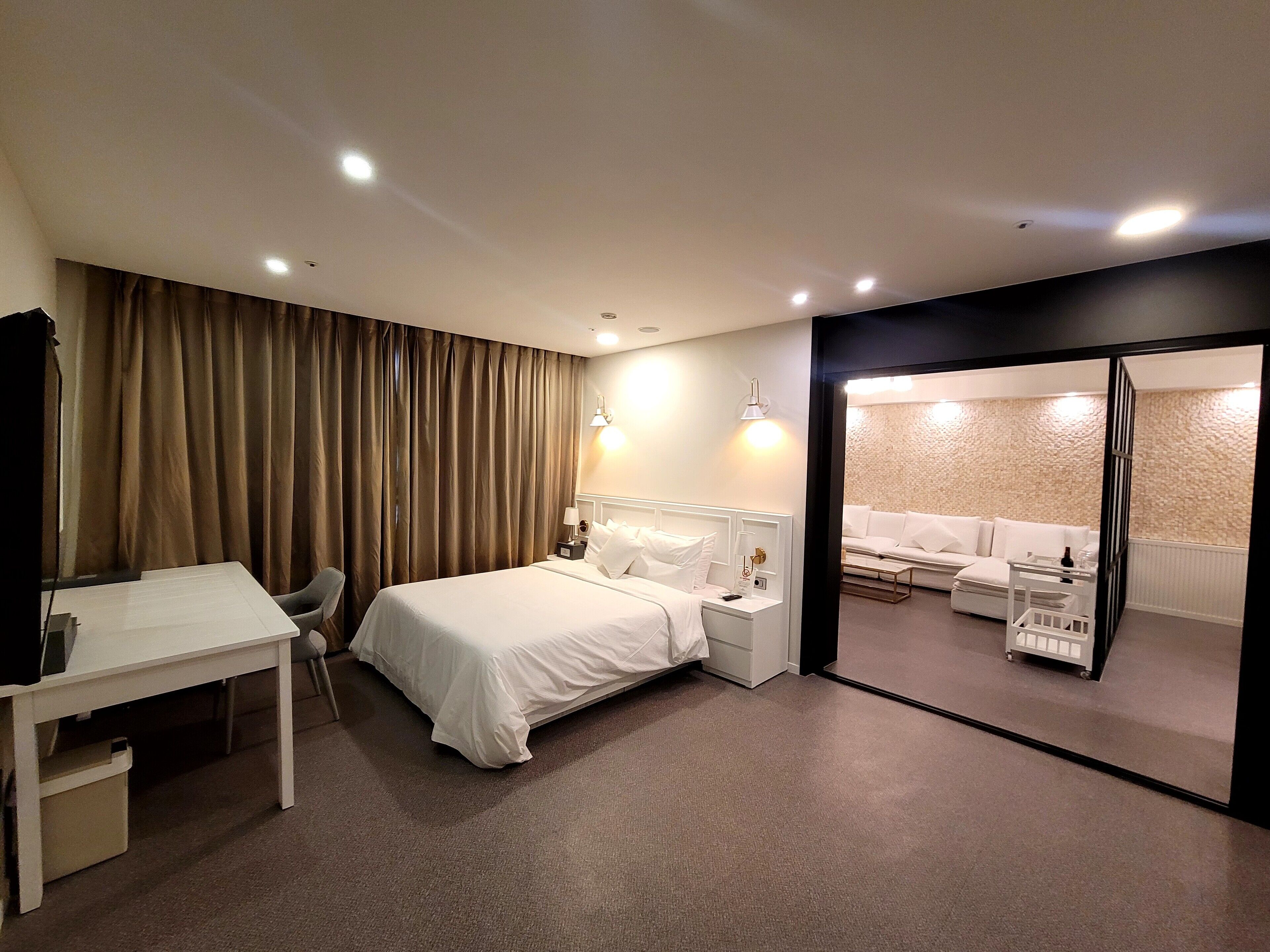 Ett hotellrum med en säng, sängbord, ett skrivbord och en sittgrupp med en soffa och fåtöljer.