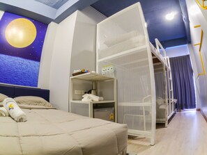 Une chambre d’hôtel avec un lit, un téléviseur fixé au mur diffusant une scène nocturne, une étagère blanche contenant des serviettes et une cloison blanche.