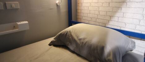 A single bed with a white mattress and a gray pillow in a room with a brick-patterned wall and a blue trim.