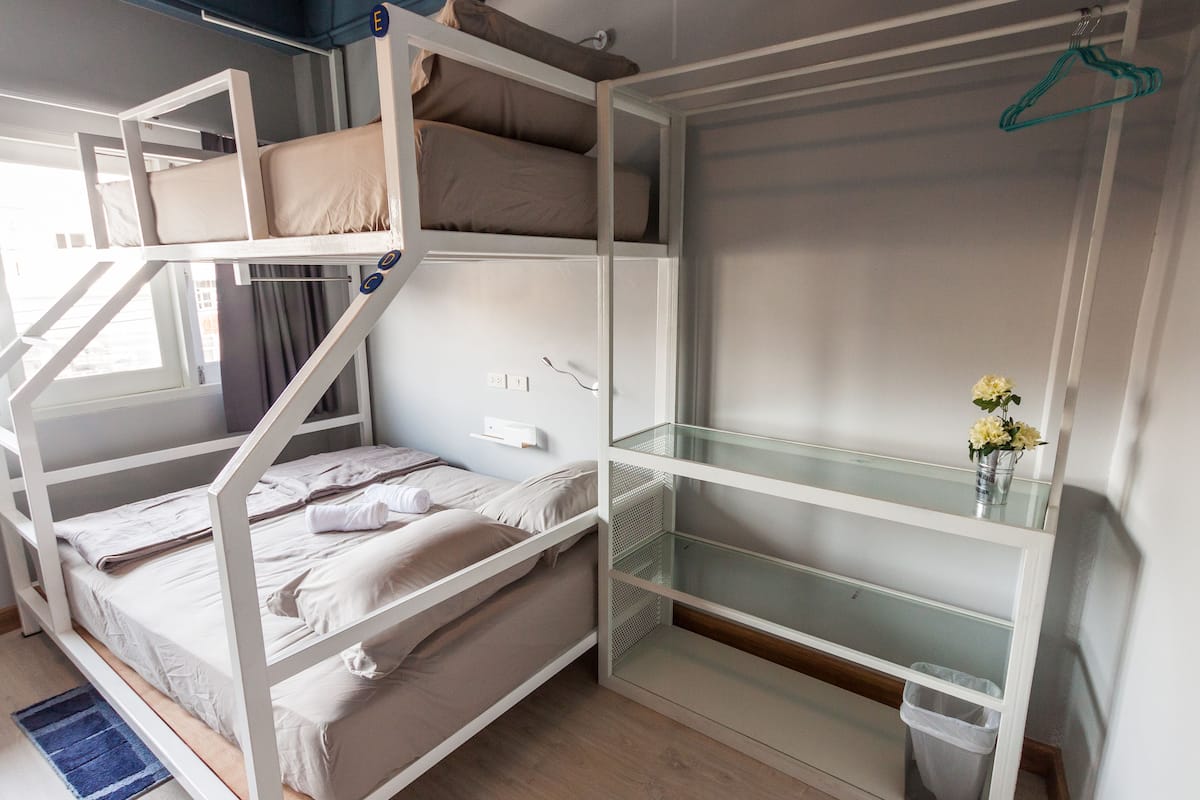 Ein Schlafzimmer mit Etagenbetten, einem Glastrennregal, einem Kleiderständer und einer kleinen Mülltonne.