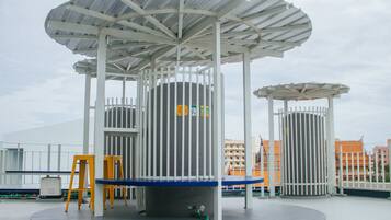 A covered outdoor seating area with a circular table and chairs, surrounded by white railings and a metal roof structure.